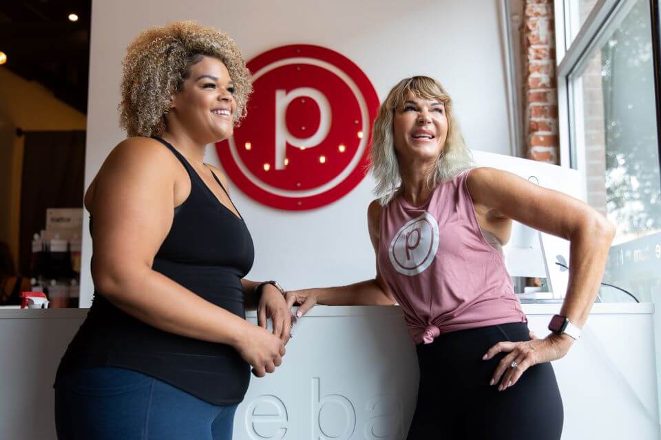 Two people smiling in front of Pure Barre front desk